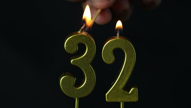 close up on the gold number thirty-second candle on a dark background.
