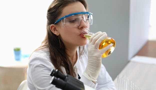 Female chimist in white protective gloves drink beer from test tube portrait. Food test concept