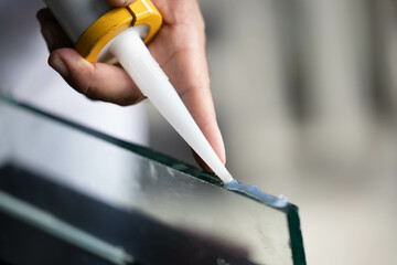 Male glass worker's hand uses silicone glue and glue to connect glass to aluminum.