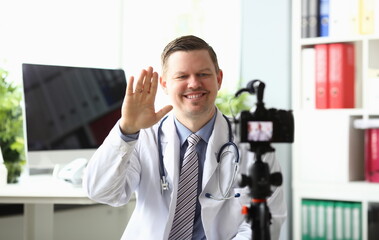 Naklejka na ściany i meble Portrait of handsome man recording medical video blog in laboratory. Smiling blogger looking at camera with happiness and waving hand. Medicine vlog concept