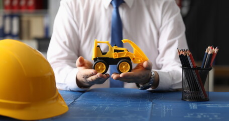 Close-up of male hands holding toy yellow excavator on palms. Builder advertising modern machines for construction business. Advertisement and car market concept © H_Ko