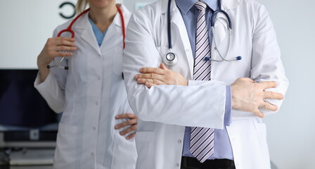 Close-up of male and female doctors standing in hospital office. Man standing with crossed arms and woman holding stethoscope. Doctors wearing white medical gowns