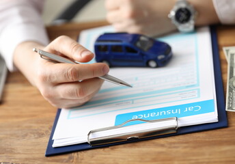 Close-up of businessman signing car insurance document on table. Blue auto model standing on paper. Collision damage waiver. Transport business and protection concept