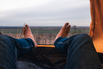 Feet of a man in a tent overlooking the green field