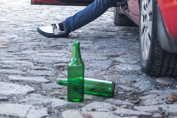 Two empty beer bottles on the floor next to the car.the driver of the car sits with the car door...