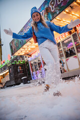 Cheerful and stylish woman, dressed in warm clothes, is having fun in a snowy winter amusement park