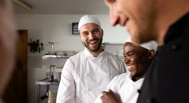 Diverse male students laughing and learning cooking from chef teacher in commercial kitchen