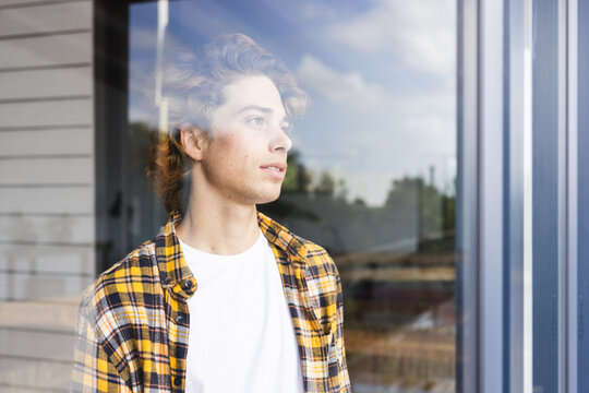 Happy caucasian man with curly hair looking through window at home