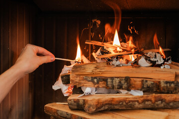Female hand holds a matchstick, ready to ignite the firewood in a fireplace
