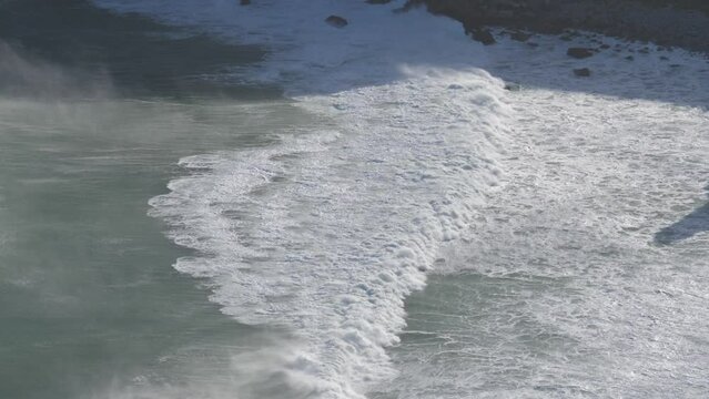 Ocean waves break into strong headwind, seen from above