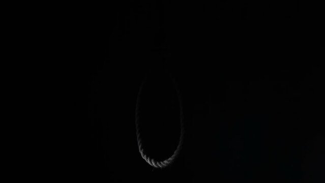 A noose of suicide rope hangs in the darkness. The light of a flashlight illuminates a loop of thick rope at night. Looping an endless video.