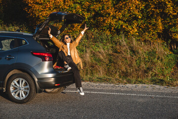 happy woman with her hands up while sitting in the trunk of her car in autumn