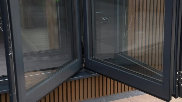 Close up shot of somebody opening sliding bi fold patio doors in slow motion on luxury wooden garden room with cladding and with reflections in the glass