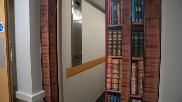 Hidden elevator door way concealed and revealed by use of fake bookcase using vinyl sticker art to hide the door inside building as the door opens