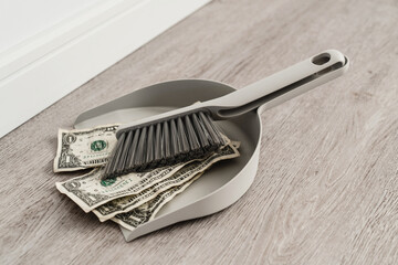 Dustpan and brush alongside scattered one-dollar bills on the floor