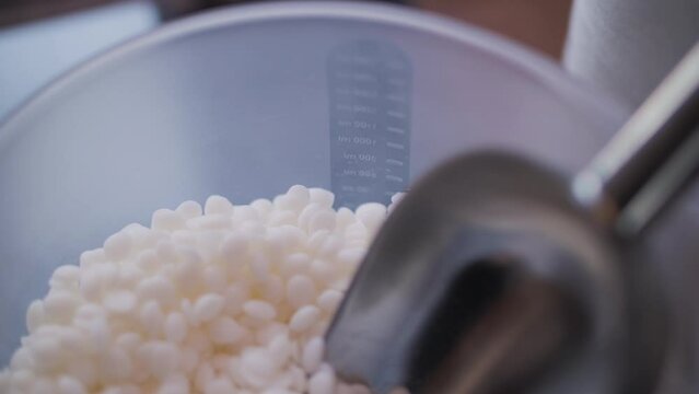 Soy wax lies in a container with a metal spoon, soy wax in the form of balls