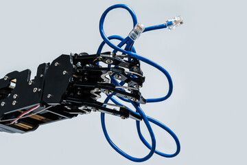 Real robot's hand holding blue Ethernet cable with rj45 connector on grey background