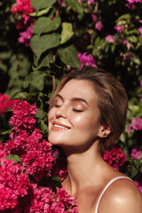 Fototapeta premium Beautiful blonde woman with smooth skin and natural makeup, as she poses against a backdrop of a bush with delicate pink flowers