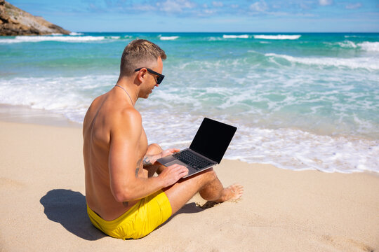 Man sitting in sand at the beach and using laptop computer