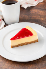 Delicious strawberry cheesecake with coffee next to it on wooden table