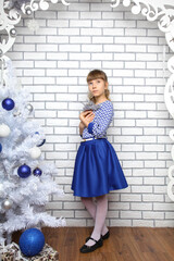 Girl in a blue dress with a Christmas tree. A girl on the background of a brick wall. New Year's photo of a teenage girl in blue and white tones.