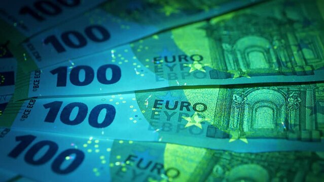 Security signs and elements on euro banknotes glows under ultraviolet light. One hundred euro banknotes under UV light