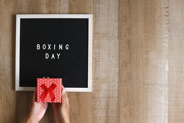 Female hands holding gift box and letter board with text Boxing Day on wooden background