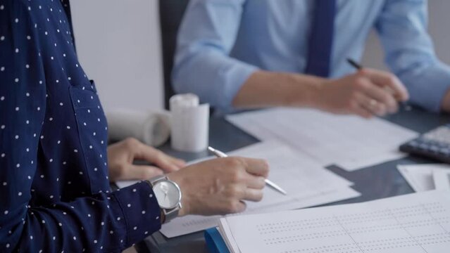 Businesspeople working at a grey glass table. Two accountants or auditors are using a calculator for counting taxes or revenue balances. Business and audit concept