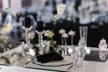 Wedding set up, dinner table reception. Serving, setting newlyweds table. Plate and glass, stack, wineglass, luxury rich decor, black napkin. Birthday, event. Restaurant interior. Side view.