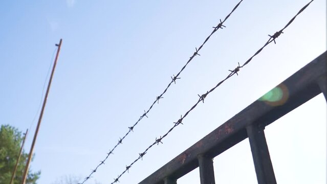 low angle view POV of wire fence above metal doors protective layer spikes two lines from entering private property valuable goods inside bright day sun shine optical flare high pole without flag tree