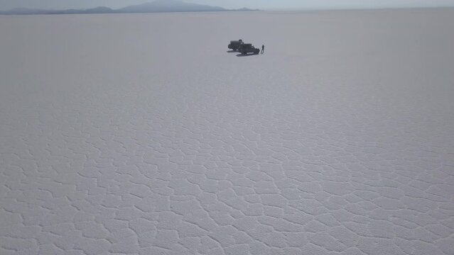 Aerial drone shot of a 4x4 offroad vehicle driving on the Salar de Uyuni salt lake around the isla pescado, fish island, on the biggest salt flat in the world in high altitude of the Andes in the Boli