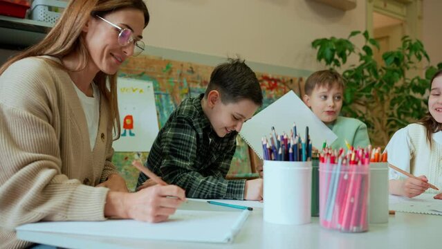 Happy female teacher paints with young students at art school