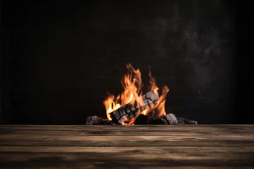 Poster Burning wood in front of wooden table with a black wall background. High quality photo © oksa_studio