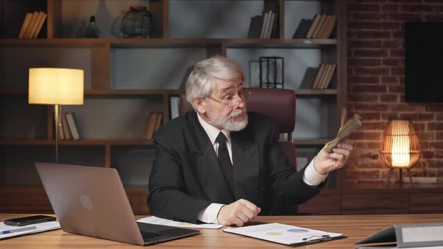 Annoyed aged male tearing up contract after demonstrating plan and cash in online conversation via laptop at work. Angry entrepreneur canceling corporate agreement because of insufficient funds.