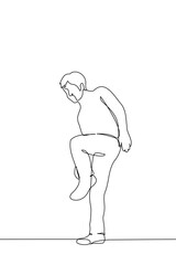 man stands on one leg adjusting his shoes or the bottom of his pants - one line art vector. concept man stopped to check clothes