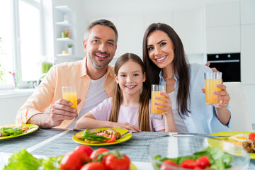 Photo of excited pretty wife husband little girl drinking fresh juice eating tasty breakfast indoors apartment kitchen