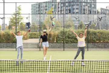 Young tennis trainer in activewear holding racket held by one of two cute girls while consulting her during individual training on stadium
