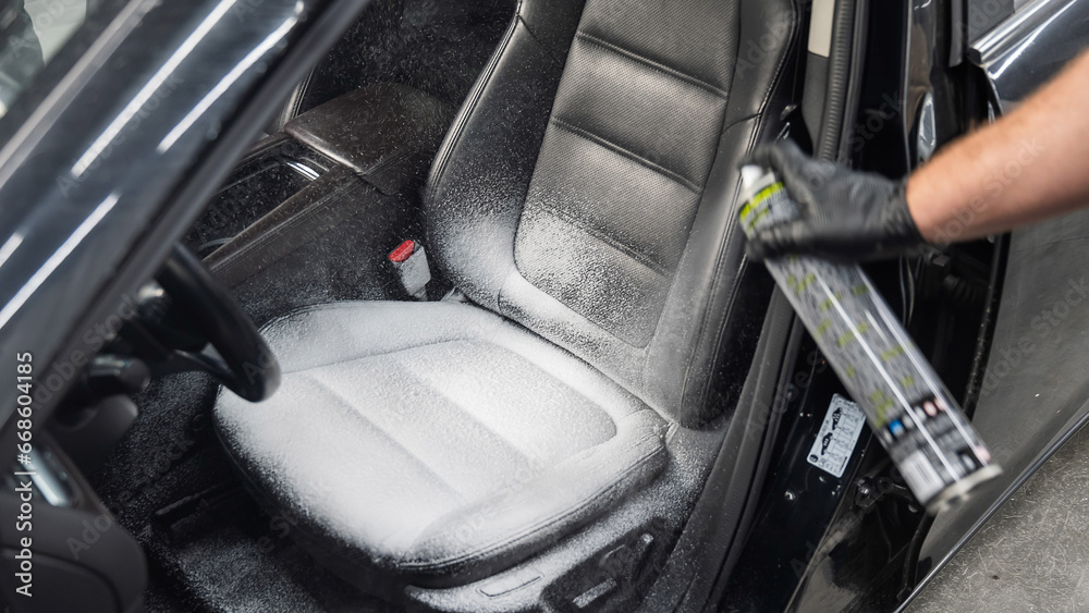 Wall mural A man cleans leather car seats with foam.