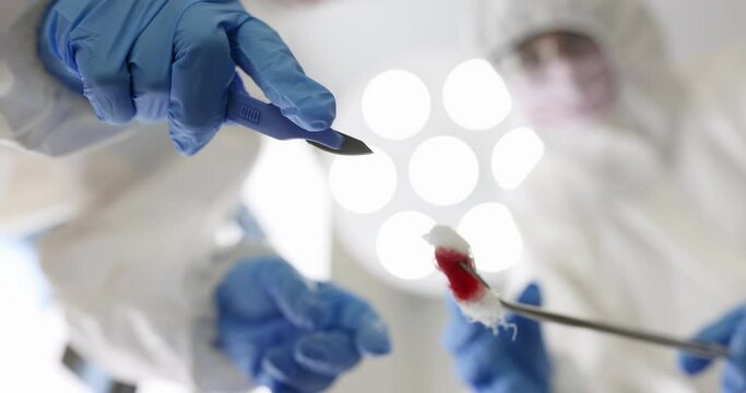 Two surgeons in protective suits hold scalpel and cotton pad with blood over a patient. Surgical operations concept