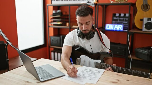 Young arab man musician playing electrical guitar composing song at music studio