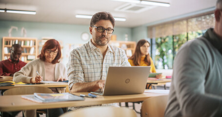 Obraz premium Middle-Aged Man Studying in Classroom, Using Laptop to Write Down Lecture Notes. Group of People Taking a Workshop on Improving Professional Soft Skills. Adult Education Center Concept