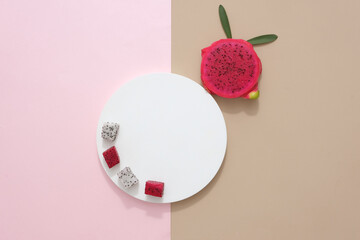 Red and white dragon fruit is displayed on a white podium, next to it is a slice of red dragon fruit and green leaves. Scenes for advertising and product design made from dragon fruit.