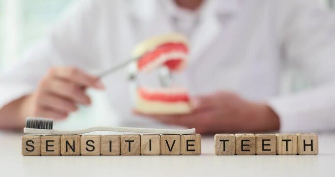 Dentist brushes teeth of artificial jaw model and word sensitive teeth. Increased tooth sensitivity