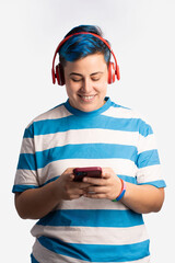Gay woman enjoying music - Non-binary person with vibrant blue hair, wearing headphones, listens to music on their smartphone, displaying a peaceful and contented expression.
