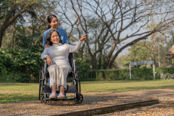 Happy nurse and elderly woman sitting in wheelchair enjoying outdoor. Beautiful nurse with senior woman in wheelchair at outdoor park. Smiling disabled old lady in wheelchair at park.