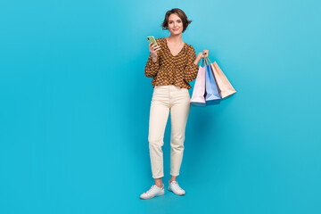 Full length photo of gorgeous person hold shop bags use smart phone eshopping isolated on blue color background