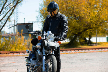 motorcyclist biker in a leather jacket and helmet on a classic chopper motorcycle in autumn