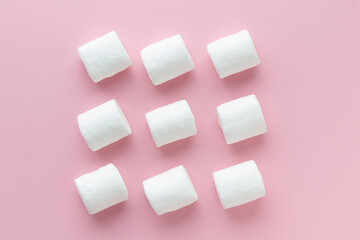 Rows of white marshmallows pattern on light pink table background in hard light. Pastel color