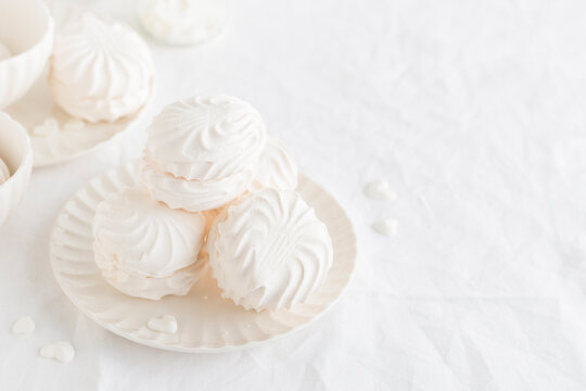 White airy zephyr or marshmallow shells on a plate on a white table, banner with space for text
