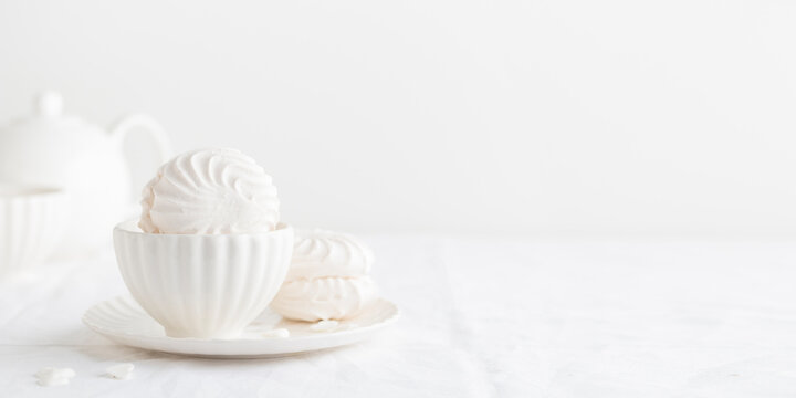 White airy zephyr or marshmallow shells on a plate on a white table, banner with space for text